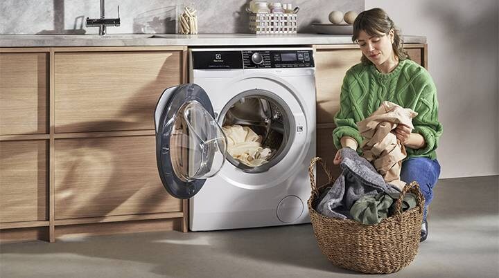 Woman in green sweater with laundry basket in front of open washing machine